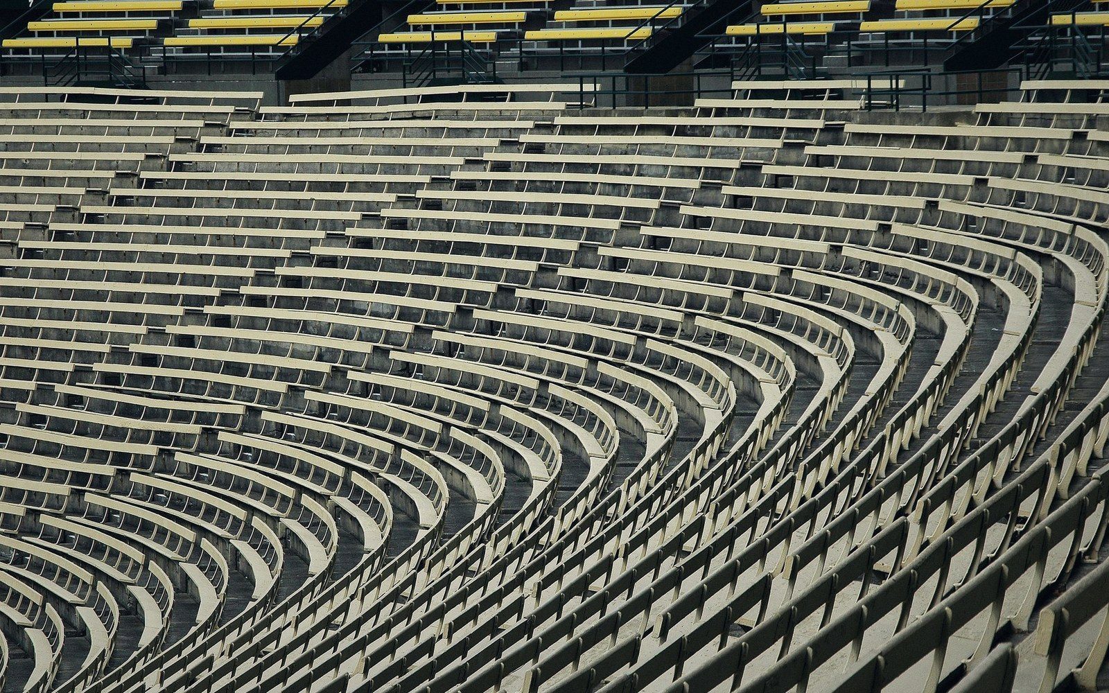 Empty stadium seating tiers photographed from pitch level at dawn, no spectators, pale light across concrete