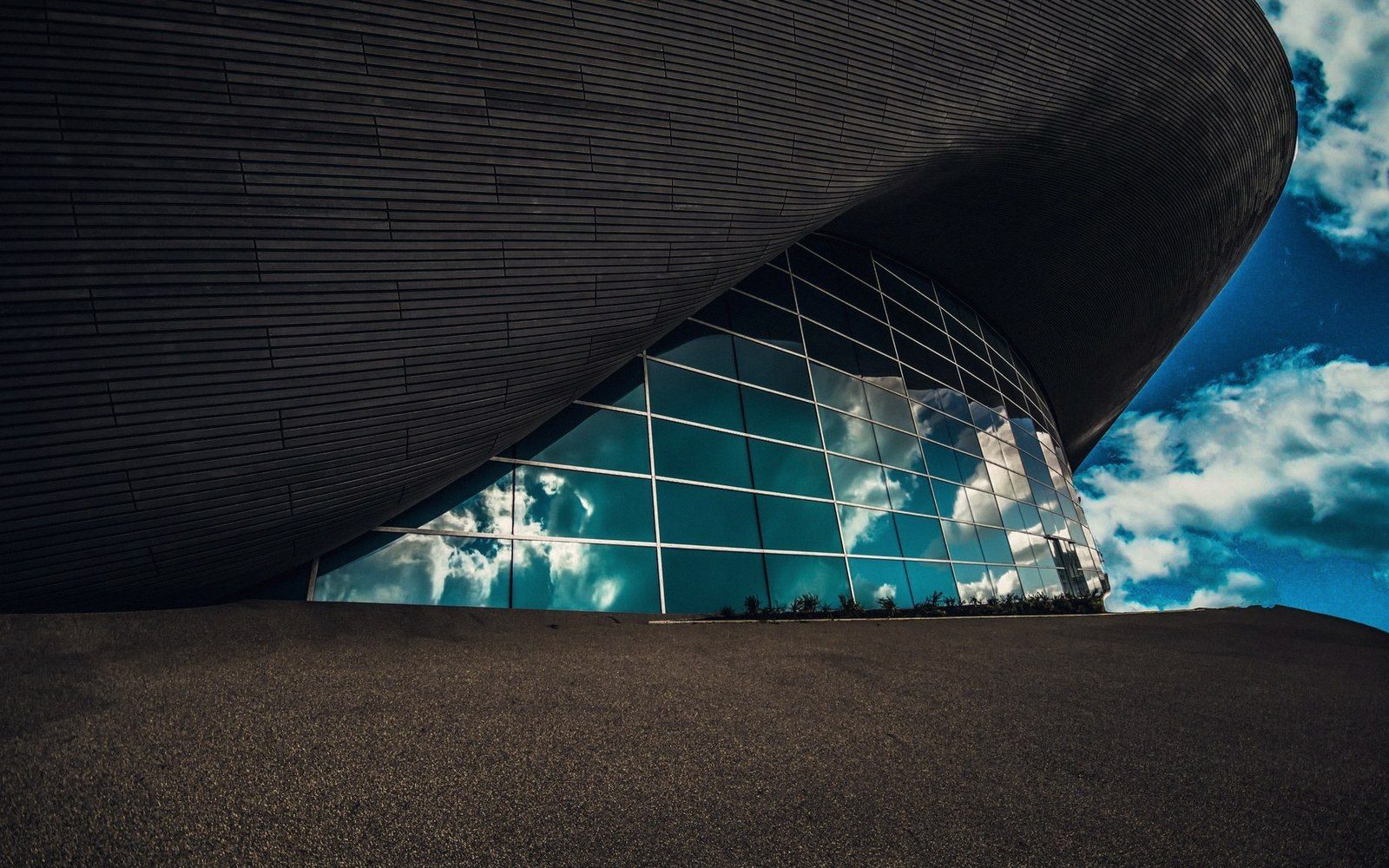 Curved roof of a modern building with clouds reflected in its angled glass facade