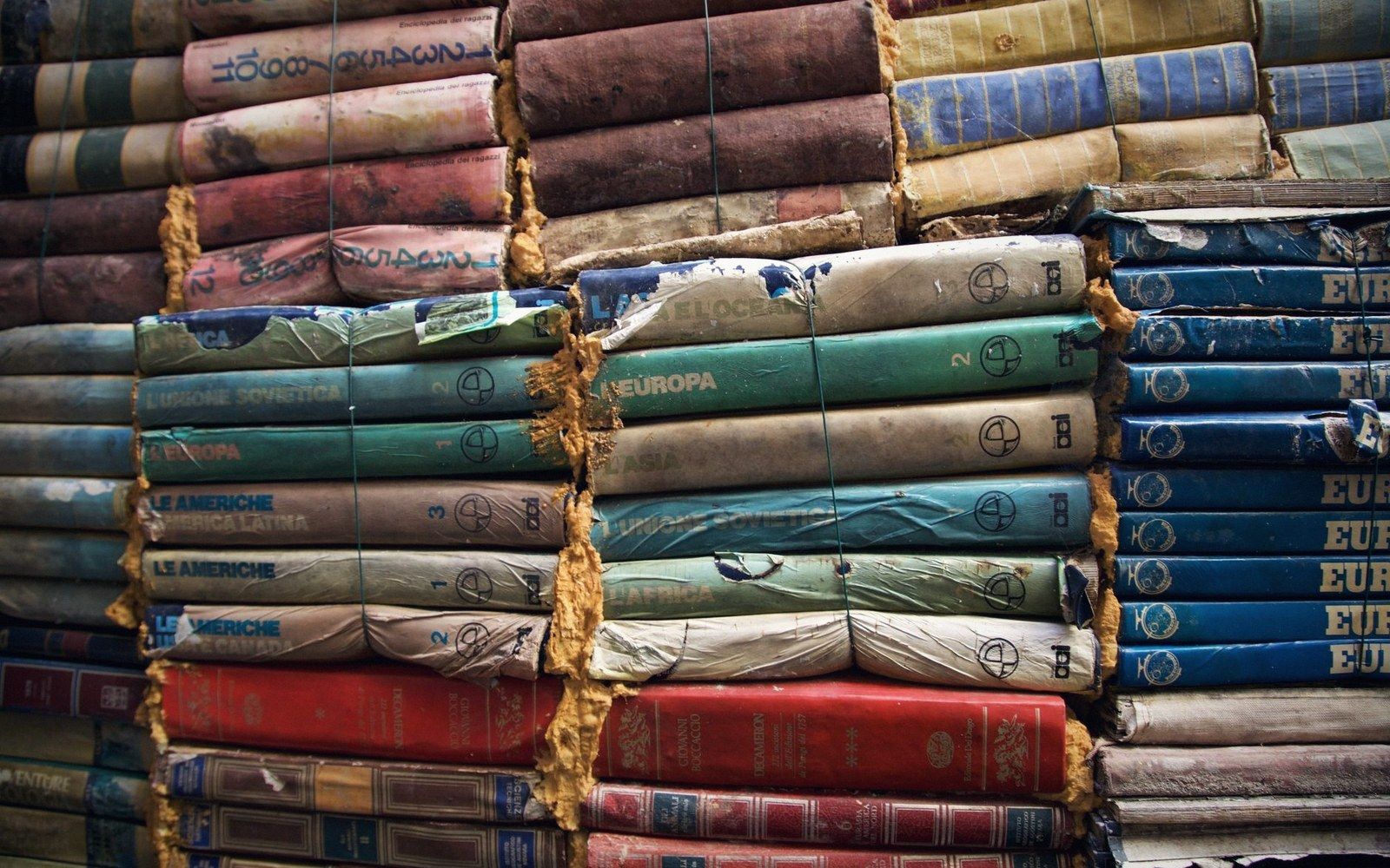 Stacks of worn hardcover encyclopedia volumes with faded, torn spine labels