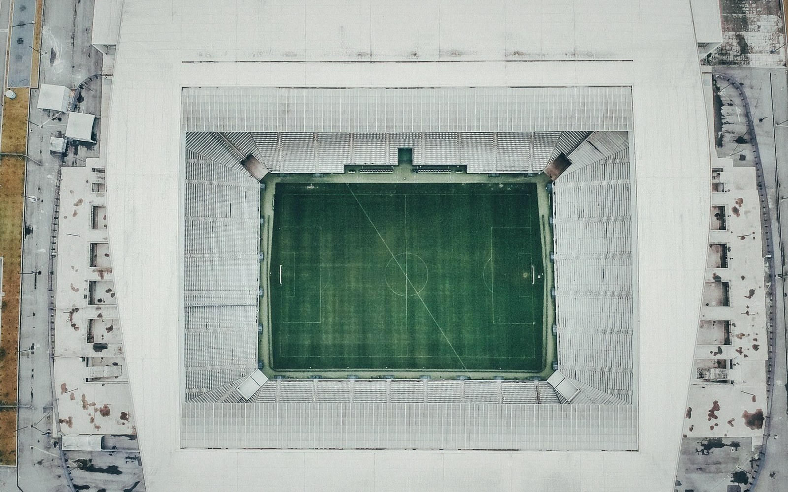 Aerial view of an empty football stadium with a green pitch and white seating tiers