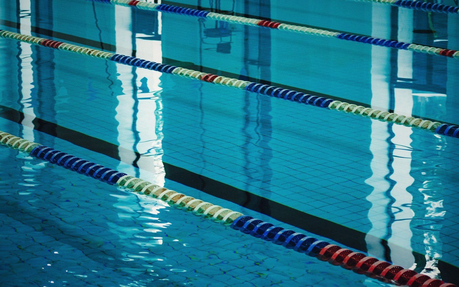 Indoor competition pool shot from the blocks end, lane ropes in place, no swimmers, blue water under fluorescent light